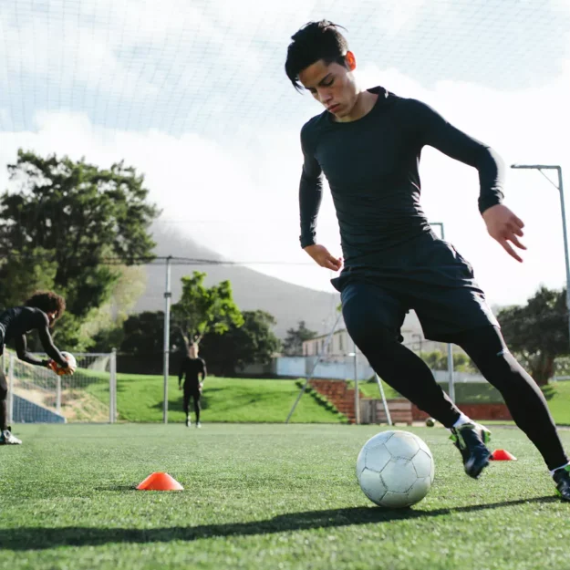 Teenage Boy Playing Football On A Pitch